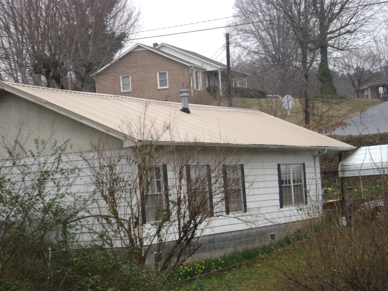 Tan metal roof on a white sided house set into a hillside in Chelsea